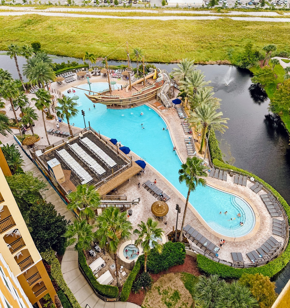 The entire pool complex seen from a guest suite balcony — pirate ship pool, relaxation pool, and the fountain pond beyond