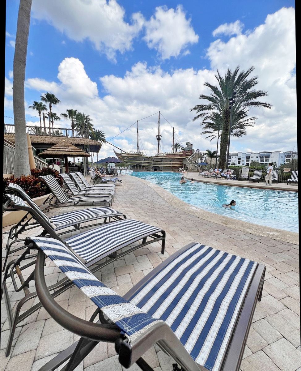 Striped blue and white poolside loungers stretching toward the pirate ship pool