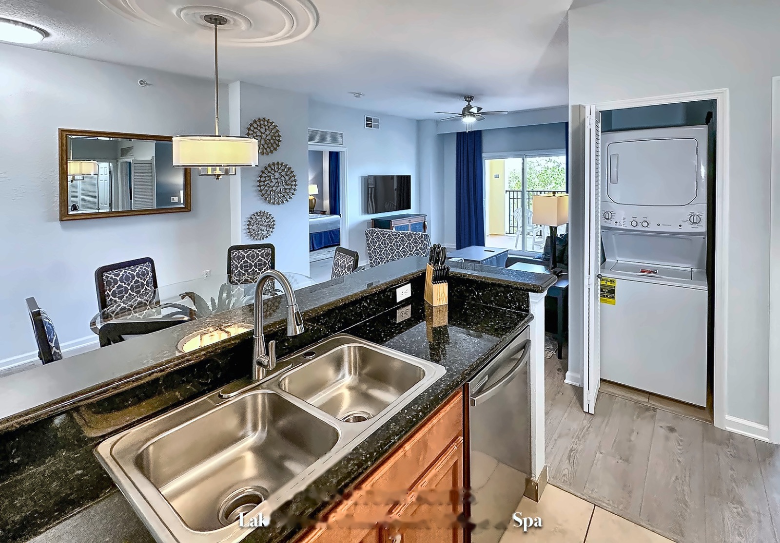 In-suite stacked washer and dryer beside the LBV suite kitchen, with the living room visible in the background