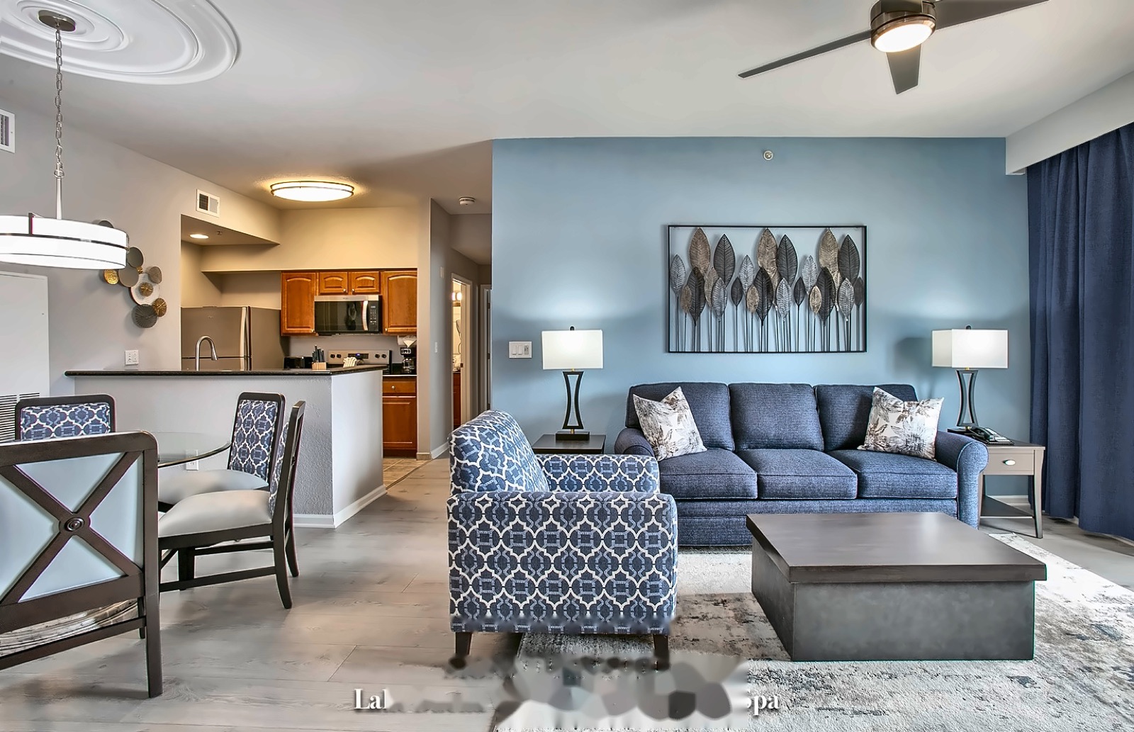 Open-concept LBV suite living room with a full sofa, accent chair, and dining area, with the kitchen visible in the background